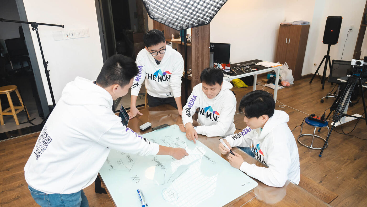 Nhân viên MONA mặc hoodie phác thảo ý tưởng trên bàn kính trong studio